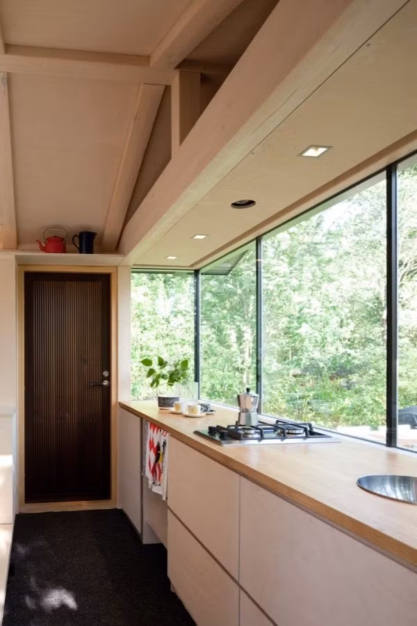 Kệ bếp và bếp ga âm được bố trí ở phần cuối nhà với bồn rửa nhỏ gọn và tiện nghi. Gia chủ đã thiết kế tủ bếp ở phía dưới kệ bếp để cất trữ tất cả đồ dùng trong bếp. Cửa kính được bố trí bao quanh bếp giúp căn bếp lúc nào cũng sáng sủa mà không cần bật điện.