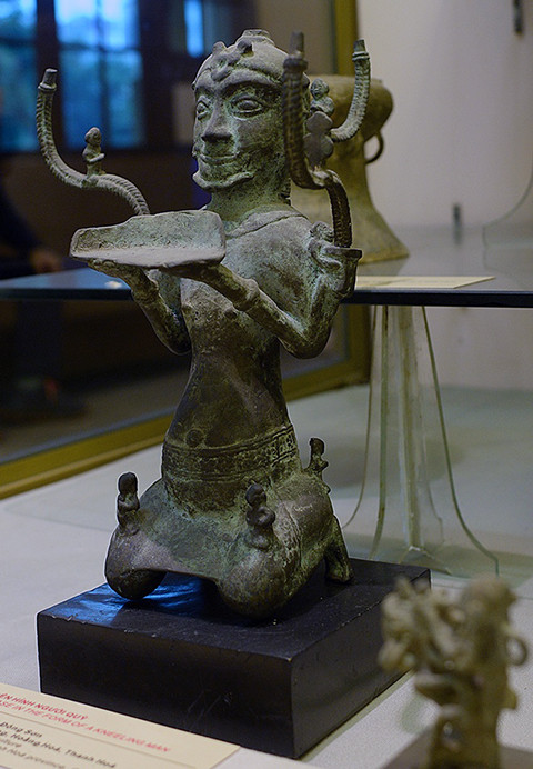 Cây đèn hình người quỳ là một trong 30 hiện vật đầu tiên được Thủ tướng công nhận là bảo vật quốc gia. Đèn cao 40 cm, rộng 27 cm, nặng 1,9 kg, có niên đại khoảng 1.700-2.000 năm. Cây đèn được phát hiện trong ngôi mộ số 3 ở Lạch Trường (Thanh Hóa), mang hình tượng một người đàn ông mình trần, đóng khố, hai tay nâng đĩa đèn trong tư thế quỳ. Trên đầu tượng được gắn vương miện, tóc để chỏm. Hai vai và sau tượng gắn 3 chữ S, mỗi chữ S đỡ một đĩa đèn và gắn một hình người đang quỳ. Trên hai đùi và đằng sau người đàn ông có 4 nhạc công cũng ở tư thế quỳ, hai nhạc công đang thổi sáo. Đây là cây đèn hình người lớn nhất trong số ít cây đèn cùng loại, thể hiện kỹ thuật đúc khéo léo và phản ánh thẩm mỹ cao của cư dân cổ thời kỳ hậu văn hóa Đông Sơn, là một trong số những bảo vật quốc gia của Việt Nam quý hiếm nhất. Cây đèn hình người quỳ là một trong 30 hiện vật đầu tiên được Thủ tướng công nhận là bảo vật quốc gia. Đèn cao 40 cm, rộng 27 cm, nặng 1,9 kg, có niên đại khoảng 1.700-2.000 năm. Cây đèn được phát hiện trong ngôi mộ số 3 ở Lạch Trường (Thanh Hóa), mang hình tượng một người đàn ông mình trần, đóng khố, hai tay nâng đĩa đèn trong tư thế quỳ. Trên đầu tượng được gắn vương miện, tóc để chỏm. Hai vai và sau tượng gắn 3 chữ S, mỗi chữ S đỡ một đĩa đèn và gắn một hình người đang quỳ. Trên hai đùi và đằng sau người đàn ông có 4 nhạc công cũng ở tư thế quỳ, hai nhạc công đang thổi sáo. Đây là cây đèn hình người lớn nhất trong số ít cây đèn cùng loại, thể hiện kỹ thuật đúc khéo léo và phản ánh thẩm mỹ cao của cư dân cổ thời kỳ hậu văn hóa Đông Sơn, là một trong số những bảo vật quốc gia của Việt Nam quý hiếm nhất.