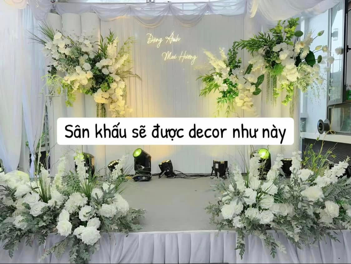 Sân khấu cũng được gia chủ mong muốn trang trí cùng tone với rạp cưới khi có 2 cụm hoa ở 2 bên sân khấu cùng 2 cụm hoa trên background.