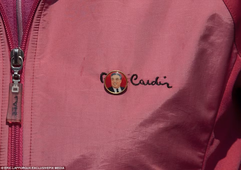 Theo nhiếp ảnh gia Lafforgue, vào năm 2008 khi lần đầu tiên đến thăm Triều Tiên, tất cả mọi người đều mặc đồng phục giống hệt nhau, trông chẳng khác gì robot. Thế nhưng hiện tại, hàng may mặc nhái các nhãn hiệu nước ngoài đã nhan nhản ở nơi đây. Trong ảnh là người phụ nữ đang mặc một chiếc áo gió màu hồng kiểu Mỹ, đeo trên ngực chiếc huy hiệu của lãnh tụ Kim Il-Sung. (Nguồn Dailymail)