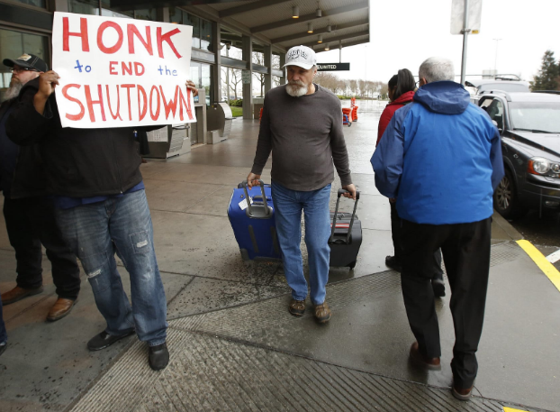 Người đàn ông mang hành lý đi qua những người biểu tình kêu gọi Tổng thống Mỹ Donald Trump và các nghị sĩ chấm dứt tình trạng chính phủ đóng cửa, ở Sacramento, bang California, ngày 16/1/2019. Ảnh: AP.