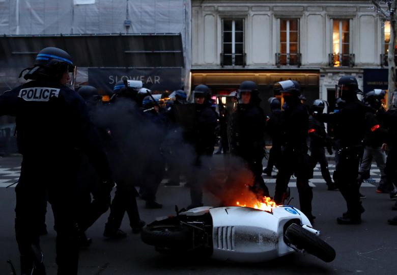 Cảnh sát chống bạo động Pháp bao vây một chiếc xe máy đang bốc cháy ngùn ngụt.