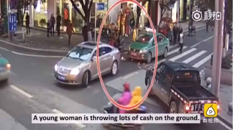 Những hình ảnh từ camera cho thấy người phụ nữ vừa bước qua vạch kẻ dành cho người đi bộ vừa thò tay vào túi xách, bốc từng nắm tiền rồi thả xuống đường. Ảnh chụp màn hình