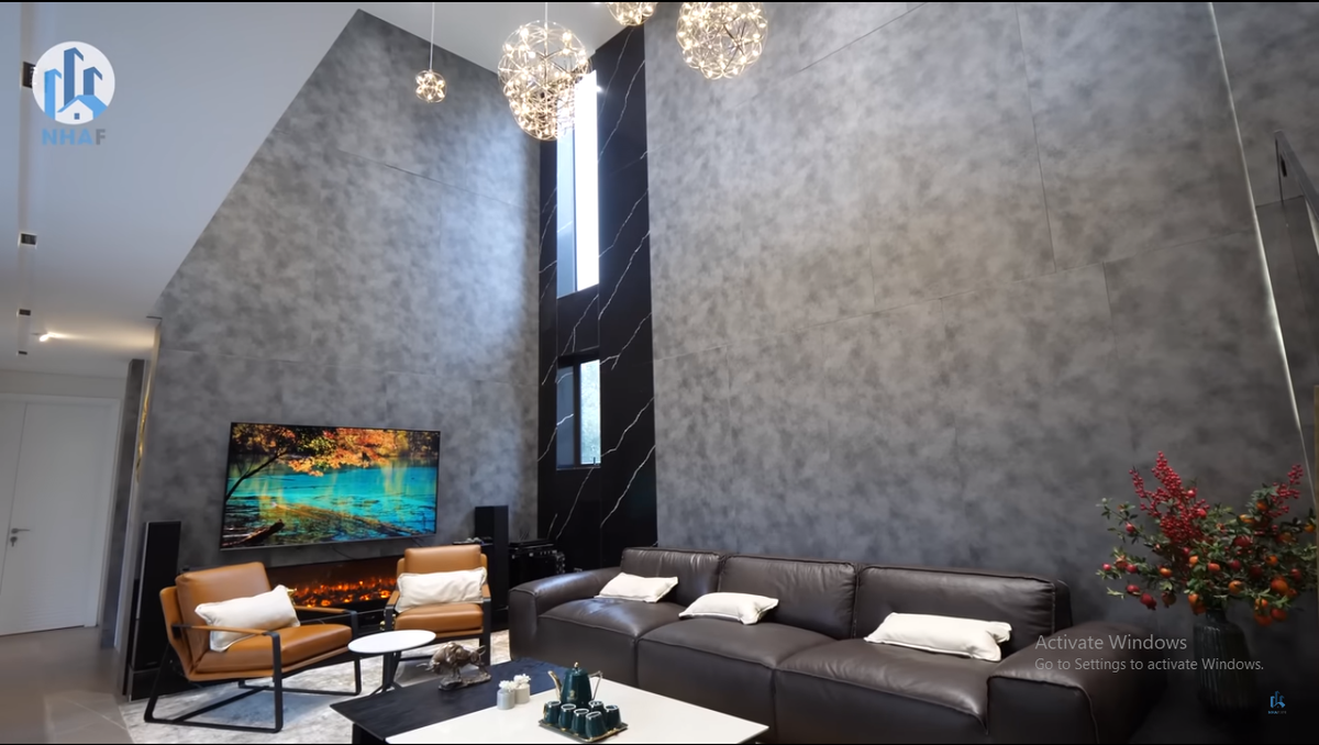 Bên trong, khu vực phòng khách có thiết kế thông tầng và sử dụng đan xen các loại vật liệu gồm: gạch dưới sàn, tường kết hợp gỗ công nghiệp và đá ốp.