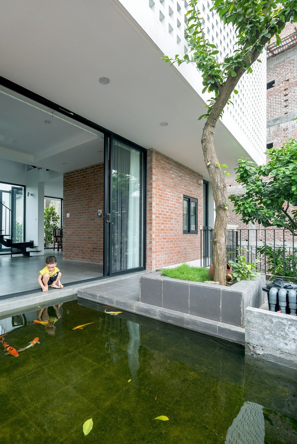 Kiến trúc sư tạo nên một không gian hiên phía trước, dẫn lối chính vào phòng khách là hành lang kết nối với mặt nước, cây xanh và những chú cá tung tăng bơi lội.