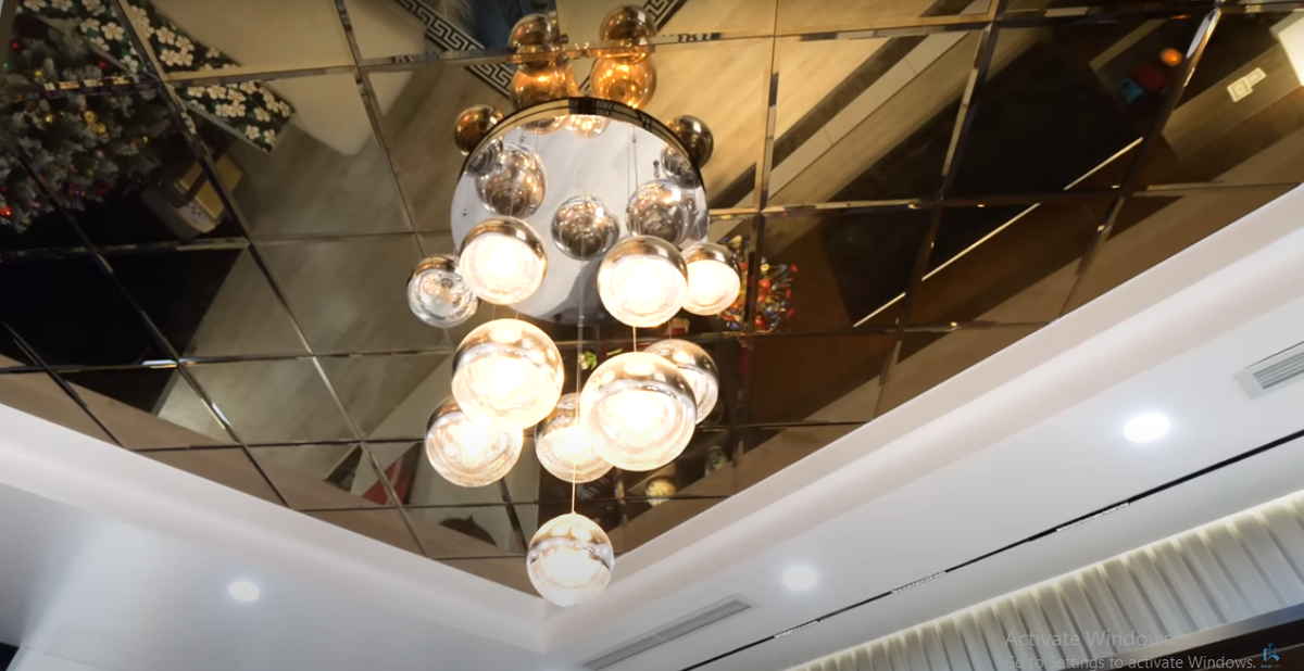 Trên trần nhà sử dụng tấm gương lớn cho không gina rộng rãi hơn. Kết hợp với đèn chùm, không gian phòng khách thêm ấm cúng.