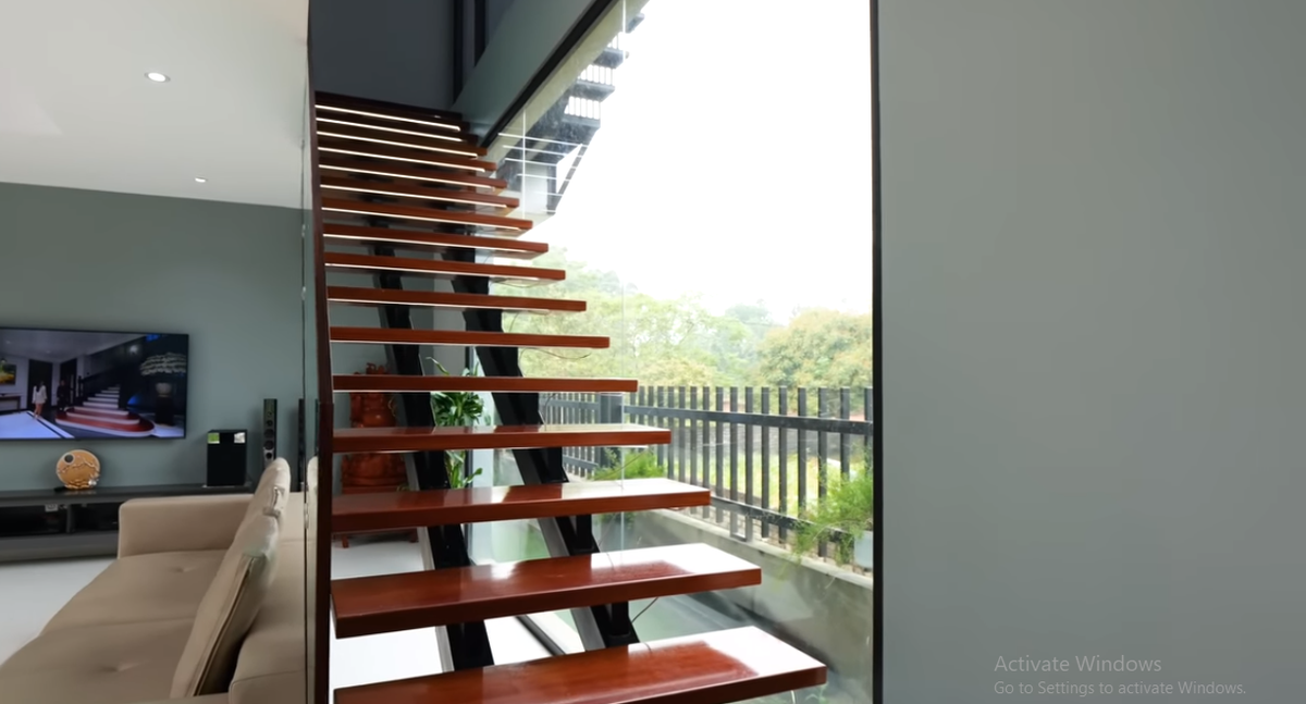 Dẫn lên tầng 2 và tầng 3 trong nhà là cầu thang khung thép, bậc thang bằng gỗ và lan can kính, phù hợp với phong cách hiện đại của căn nhà.