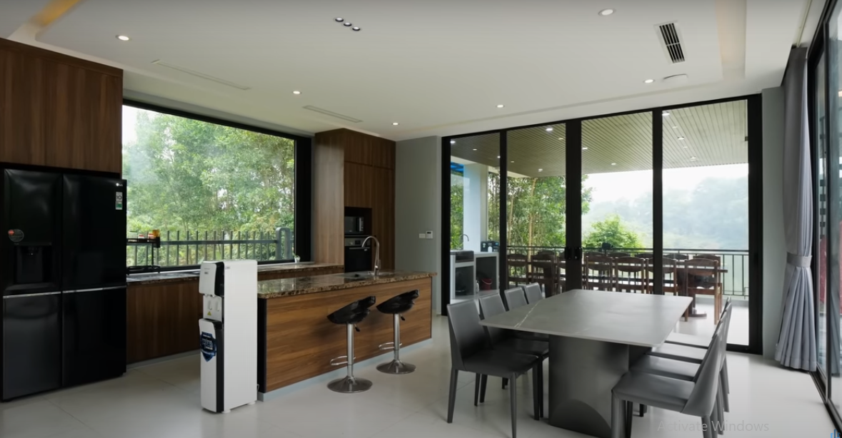 Đối diện khu vực tiếp khách là bếp và bàn ăn. Xung quanh đều là những ô cửa kính lớn, giúp gia chủ thoả sức ngắm cảnh bên ngoài ở mọi góc.