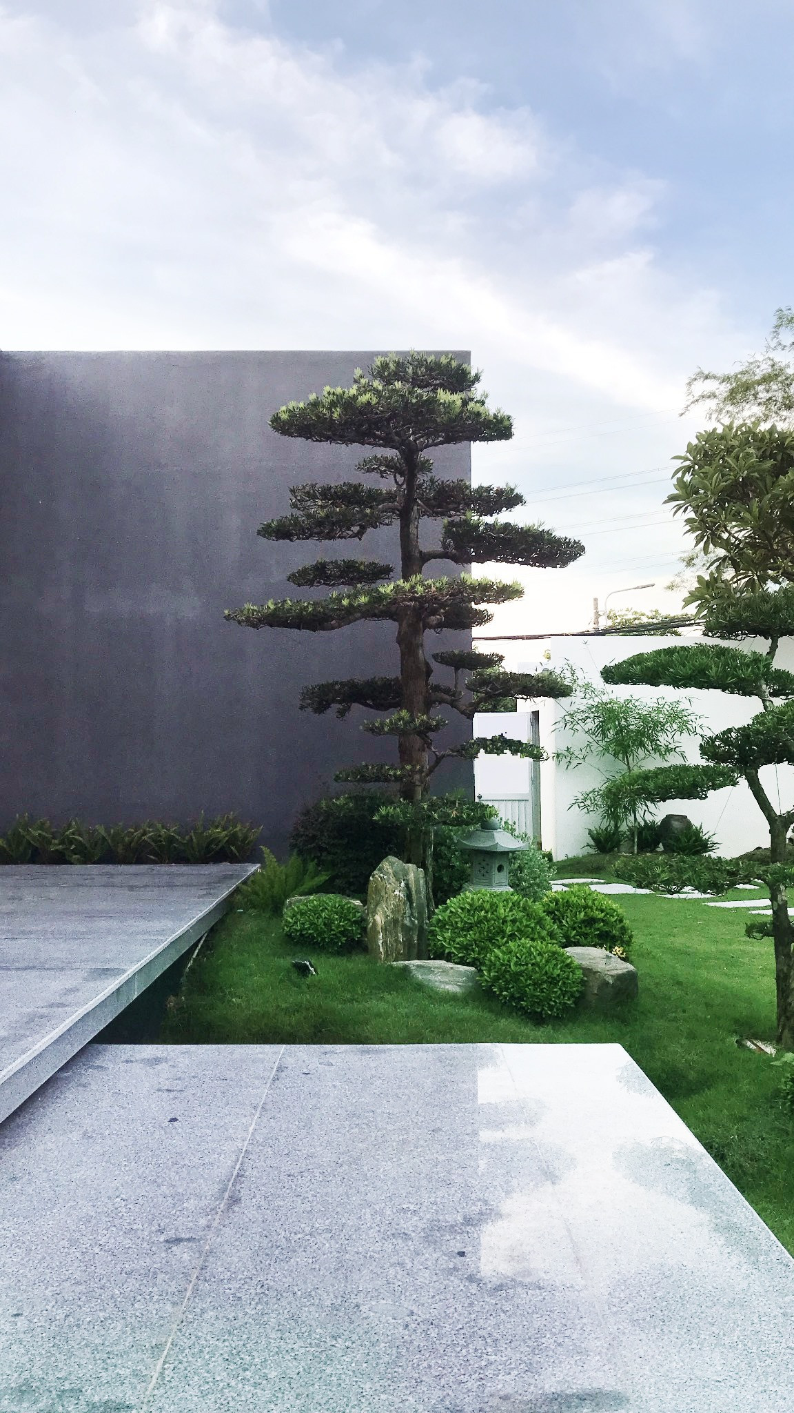 Bên ngoài căn nhà rợp bóng mát với thảm cỏ xanh mướt và hệ cây cảnh được cắt tỉa dẹp mắt.