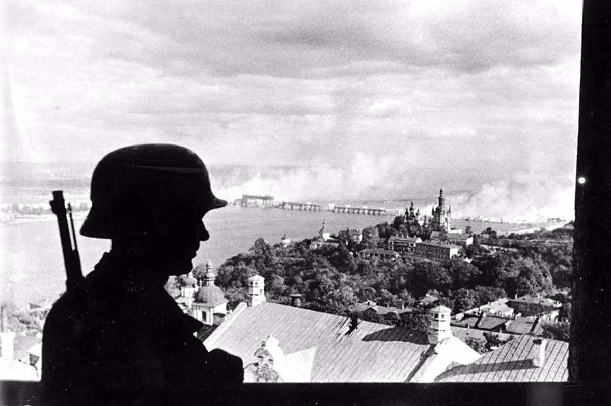 Binh lính Đức quốc xã quan sát tình hình ở Kiev năm 1941. Phía xa là cầu bắc qua sông Dnieper bốc khói nghi ngút sau khi bị phá hủy trong thời gian diễn ra chiến sự ác liệt.