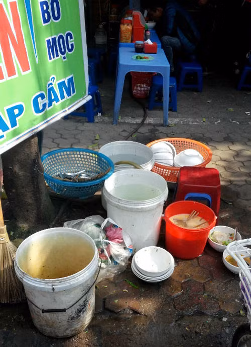 Xô nước rửa bát ngàu bọt vàng. Chiếc thùng chứa nước rửa cũng đầy ruồi bu. Nếu tận mắt nhìn khu rửa bát của quán bún như thế này ai cũng phải kinh hãi.