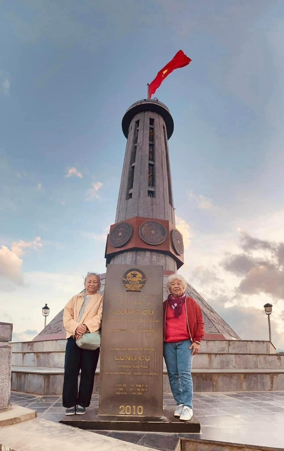 Tới nơi, đôi bạn phải leo gần 300 bậc thang để tới điểm chụp hình với cột cờ. Trong khi bà Lý có sức khỏe tốt hơn, chân đi thoăn thoắt thì bà Lá mệt nhoài, có lúc như kiệt sức, bước từng bước chậm chạp. Tuy nhiên đến lúc check-in, ai cũng giữ cho mình nụ cười tươi trên môi. (Ảnh: Nguyễn Đức Đông)