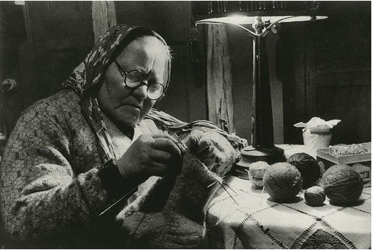 Người phụ nữ ngồi đan tất dưới ánh đèn.