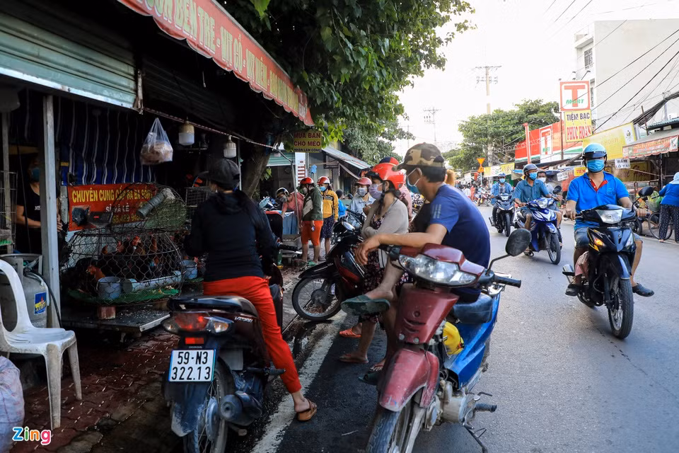 Trước một sạp bán thịt gia cầm, nhiều người đứng ngồi san sát chờ lấy hàng.