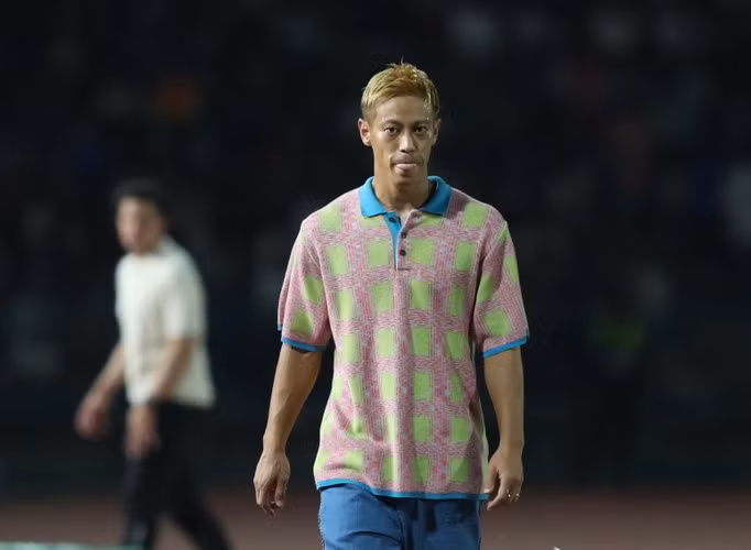 Thay vì mặc quần short như trận trước, Keisuke Honda mặc một chiếc áo polo hàng hiệu nổi bật với tông màu hồng xanh lạ lẫm phối cùng quần ống loe màu xanh dương và đôi giày lười màu cam.