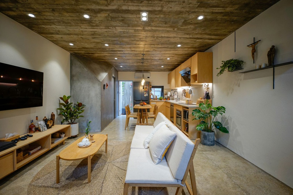 Tầng trệt là không gian của phòng khách và bếp với đầy đủ các chức năng. Khu vực này được thiết kế đơn gian với gam màu trắng, vàng của gỗ và xám xi măng là chủ đạo.