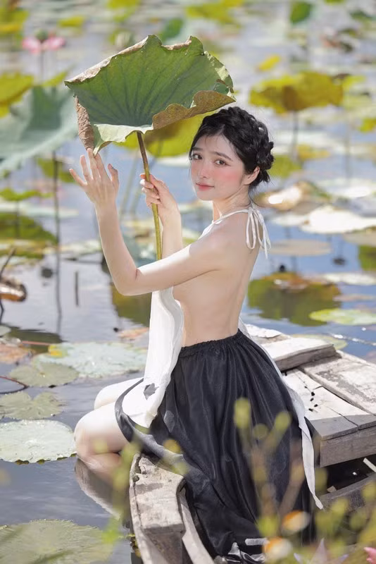 Khánh Linh diện áo yếm gam màu trắng, phối với chân váy đụp màu đen cùng kiểu tóc tết mô phỏng như khăn mỏ quạ.