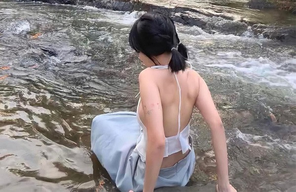 Cô mặc chiếc áo yếm màu trắng kết hợp chân váy màu xanh. Bộ đồ có chất liệu lụa mềm mại, mỏng nhẹ, tôn lên từng đường nét cơ thể.