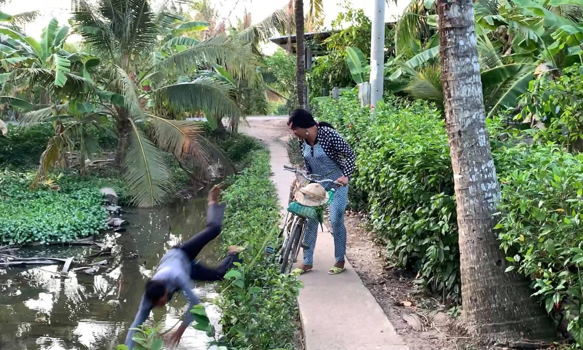 Sau khi đi qua một đoạn đường dài, đến bờ kênh thì anh chồng ngã nhào xuống. Cô vợ liền gọi mẹ chồng ra chứng kiến.