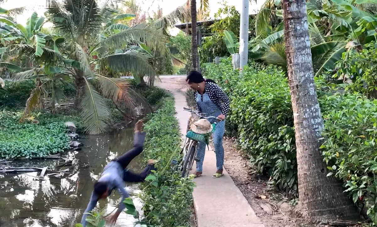 Sau khi đi qua một đoạn đường dài, đến bờ kênh thì anh chồng ngã nhào xuống. Cô vợ liền gọi mẹ chồng ra chứng kiến.