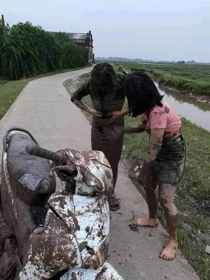 Cụ thể, xuất hiện trong hình ảnh ghi lại 2 cô gái đi chiếc xe máy màu trắng bị hư hại phần vỏ nhựa và đặc biết, người họ lấm lem toàn bùn, đất.