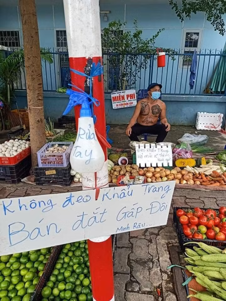 Không chỉ vậy, chủ sạp rau còn đặt thêm 2 tấm biển "đeo khẩu trang hở mũi không thêm hành ngò" và "không đeo khẩu trang bán đắt gấp đôi" trước gian hàng để khuyến khích người tới mua hàng phải đeo khẩu trang, không những thế mà còn phải đeo đúng cách.