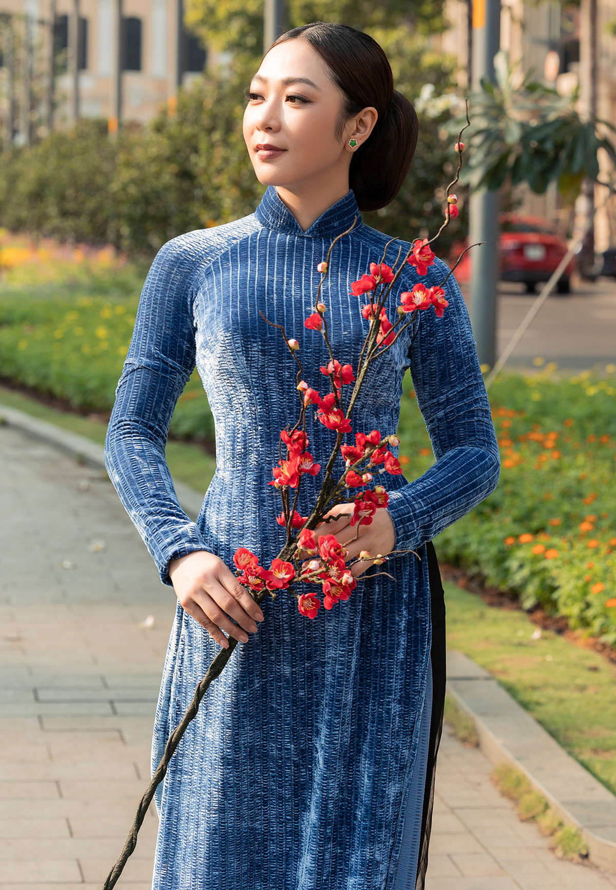 Ca sĩ 8X kết hợp áo dài với phụ kiện vòng cổ ngọc trai, kiểu tóc búi cao, tạo dáng cùng đạo cụ cành đào trong bộ ảnh mừng năm mới.