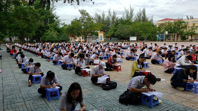 Học sinh ngồi làm bài thi trên ghế nhựa ngay dưới sân trường tại Hậu Giang.