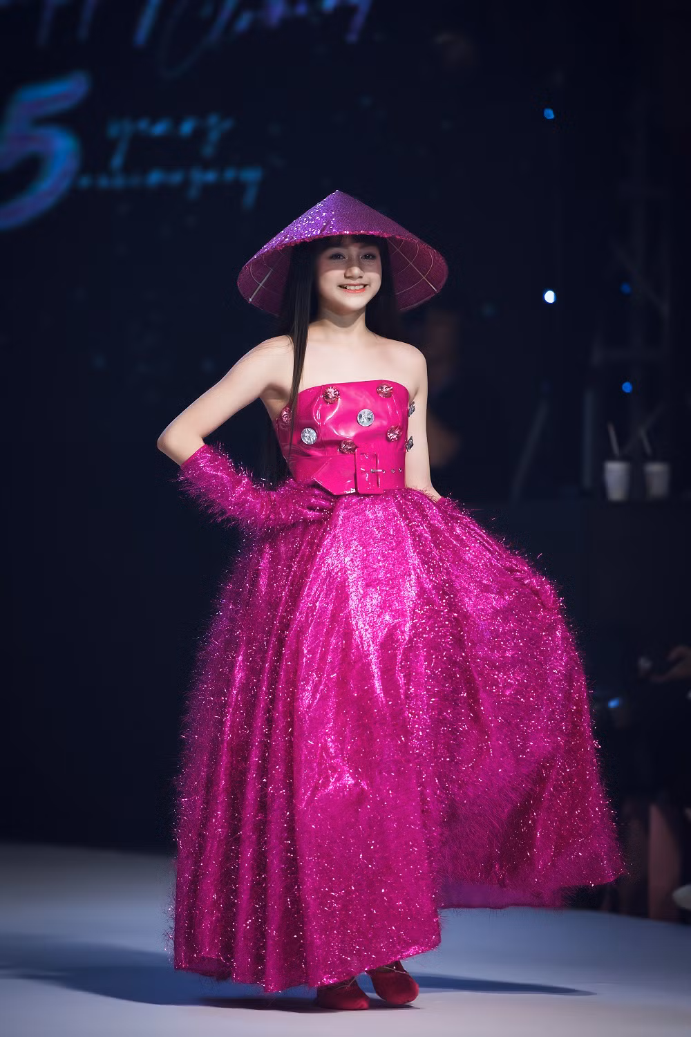 Trên sàn diễn thời trang, người mẫu nhí Ngọc Huyền xuất hiện nổi bật với trang phục cách tân màu hồng neon, kết hợp phụ kiện lấy cảm hứng từ nón lá.