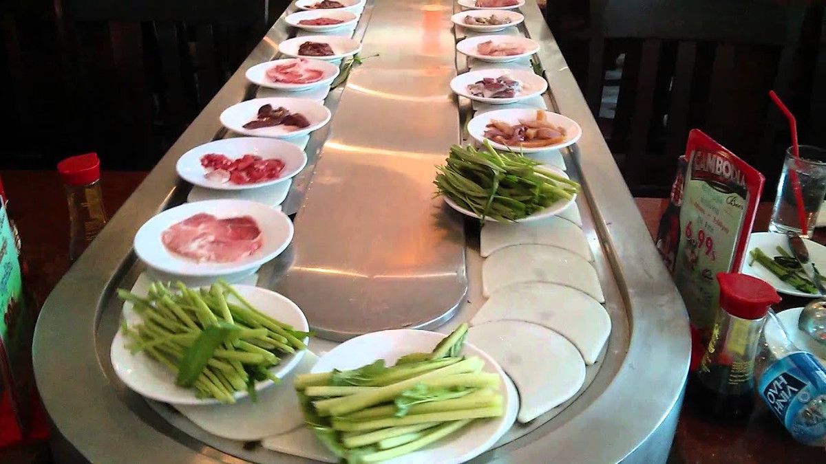 Cụ thể, chàng trai trong clip bị bàn tán liên tục lấy từ băng chuyền những đĩa thức ăn mình thích và bày biện khá nhiều trên bàn.