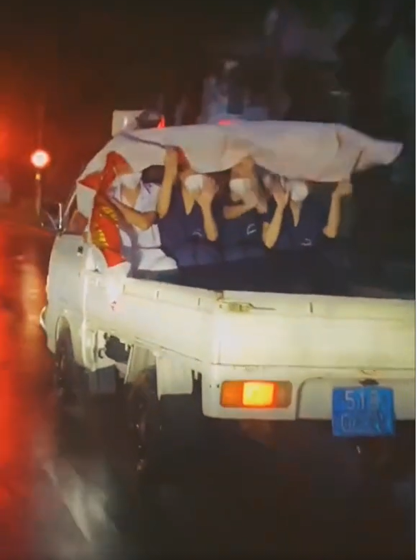 Trong video là cảnh các bạn trẻ người mặc đồng phục nhân viên y tế, người mặc áo blouse trắng đang co ro trên thùng sau của chiếc ô tô bán tải.