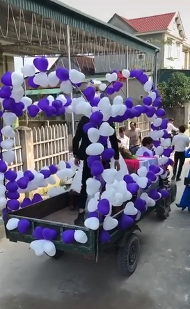 Theo đó, thay vì đón dâu bằng xe hơi trang trí hoa lá cành chỉn chu, cặp đôi này lại lựa chọn một chiếc xe... mui trần đúng nghĩa. Thật ra, cũng không biết gọi chiếc xe này là xe gì, phần đuôi thì là của xe tải loại nhỏ, phần đầu lại thô sơ như xe công nông. Nhưng sự kết hợp này cùng với những chùm bóng bay trắng - tím trang trí lại tạo nên chiếc xe hoa độc đáo cho màn rước dâu.