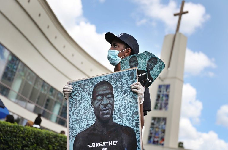 Một người tới viếng George Floyd cầm theo bức hình của anh, bên ngoài nhà thờ Fountain of Praise ở Houston ngày 8/6. Ảnh: New York Times.