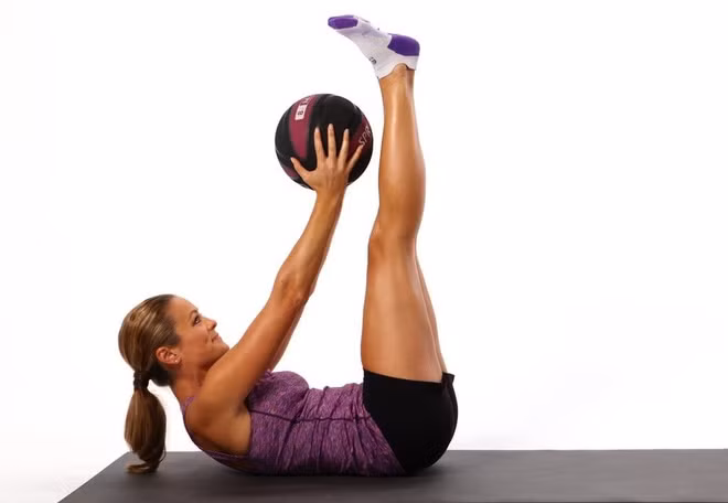 Nằm ngửa nâng cao tay chân: Bài tập này sẽ giúp cơ bụng trên săn chắc. Bạn có thể thực hiện với tạ hoặc bóng để tăng độ khó cho động tác. Cách thực hiện: Nằm ngửa, giơ 2 chân lên cao một góc 90 độ so với mặt sàn. Cánh tay giơ thẳng, đồng thời hơi nhấc vai và lưng lên khỏi sàn. Giữ một giây, sau đó, từ từ hạ thấp vai và trở về vị trí ban đầu. Luôn giữ thẳng tay và chân trong khi thực hiện. Ảnh: Verywellfit.