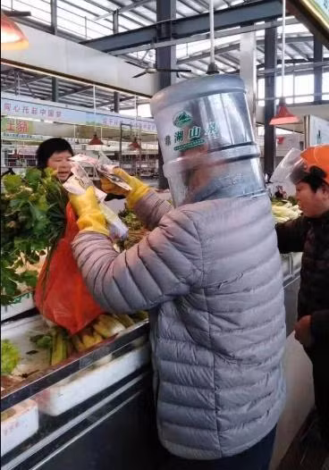 Đi găng tay cao su, đeo khẩu trang thôi vẫn chưa đủ, người đàn ông này còn đội cả một chiếc thùng nhựa hình trụ trên đầu nữa, trái ngược hoàn toàn với người bán hàng, người không đeo khẩu trang.