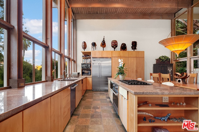 Nhà bếp rộng rãi, sáng sủa, với các trang thiết bị nấu nướng hiện đại được tích hợp trong những chiếc tủ, bàn gỗ đơn sơ, không cầu kỳ.