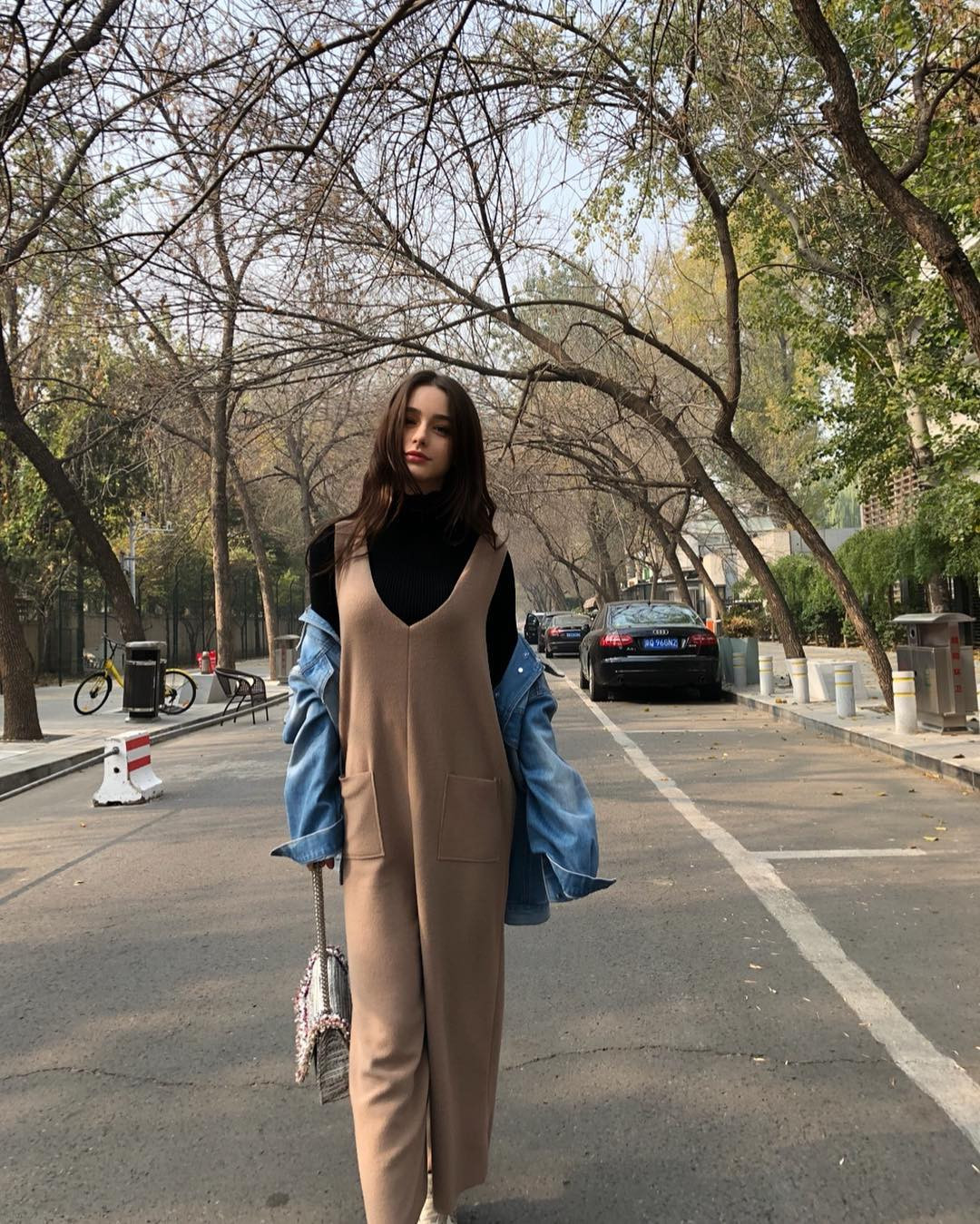 Cô người mẫu Nga mặc bộ jumpsuit màu nâu dáng hai dây to bản bên ngoài áo cổ lọ màu đen. Phối cùng với bộ đồ cô mặc áo khoác denim đeo túi xách. Với chiều cao 1m70 cô có thể tự tin mặc kiểu đồ dành cho người cao như thế này.