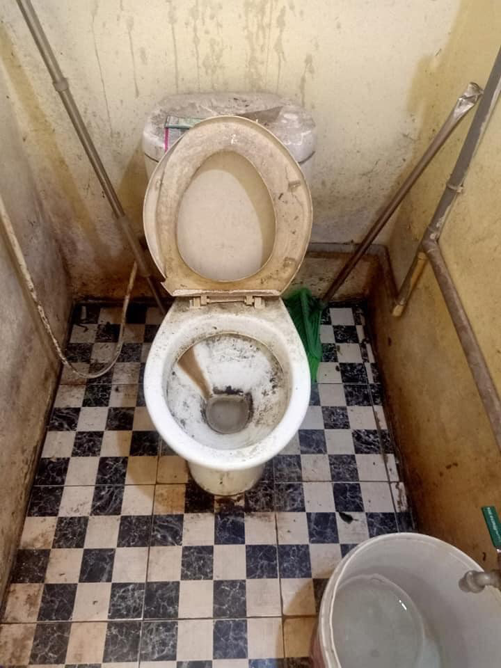 Bồn cầu bám đầy bụi đen bẩn thỉu, nắp bồn cầu vỡ nát, các bức tường xung quanh bụi bẩn đóng thành từng mảng.