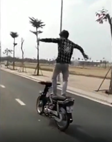 Cụ thể, khi đi đến đoạn đường vắng người, thanh niên này đứng hẳn lên yên xe, trong khi chiếc xe vẫn đang di chuyển. Khi cho rằng đã giữ được thăng bằng, thanh niên quơ tay loạn xạ như đang "diễn xiếc", đồng thời tạo dáng hình trái tim để người phía sau dùng điện thoại quay lại clip.