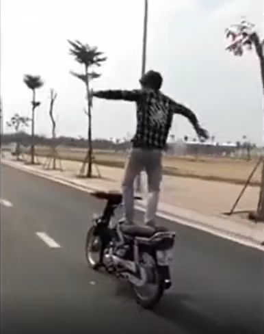 Cụ thể, khi đi đến đoạn đường vắng người, thanh niên này đứng hẳn lên yên xe, trong khi chiếc xe vẫn đang di chuyển. Khi cho rằng đã giữ được thăng bằng, thanh niên quơ tay loạn xạ như đang "diễn xiếc", đồng thời tạo dáng hình trái tim để người phía sau dùng điện thoại quay lại clip.