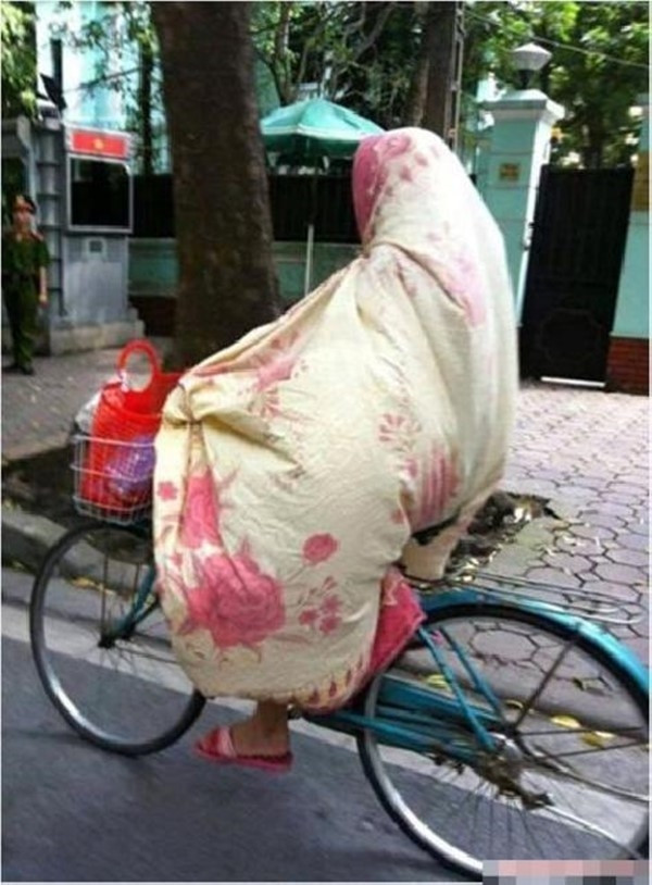Hình ảnh người phụ nữ khoác chiếc chăn chống rét điều khiển xe đạp.