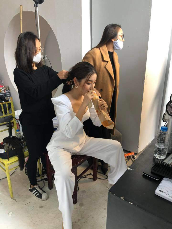 Trước khi dẫn, Huyền My tranh thủ ăn tạm bánh mì trong lúc chờ trang điểm, làm tóc. Cô nàng lựa chọn dáng ngồi hạn chế tối đa việc vụn bánh mì rơi làm bẩn bộ quần áo trắng tinh.