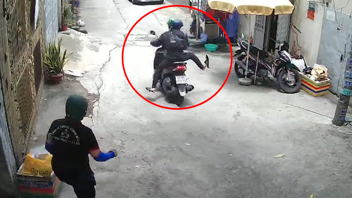 Khi dựng lại trước cửa nhà, hai thanh niên cho xe quay đầu hướng ra ngõ. Người ngồi sau bước xuống xe, tay cầm điện thoại. Cả hai vờ bắt chuyện với người phụ nữ, hỏi thăm qua loa điều gì đó.