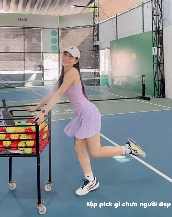 Nhật Lê nở nụ cười trong tư thế tạo dáng với 1 chân nhấc nhẹ, tay vịn vào giỏ bóng, khéo léo khoe đường cong cơ thể cuốn hút, vòng eo nhỏ nhắn.