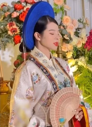 Vừa xuất hiện, cô dâu đã chiếm trọn ánh nhìn với chiếc áo tone trắng, đầu đội mấn xanh. Toàn bộ thân áo được trang trí bằng hoa văn dạng hình tròn khép kín, đan xen là những hình phượng múa cùng hoa lá đính thêm kim tuyến lấp la lấp lánh.