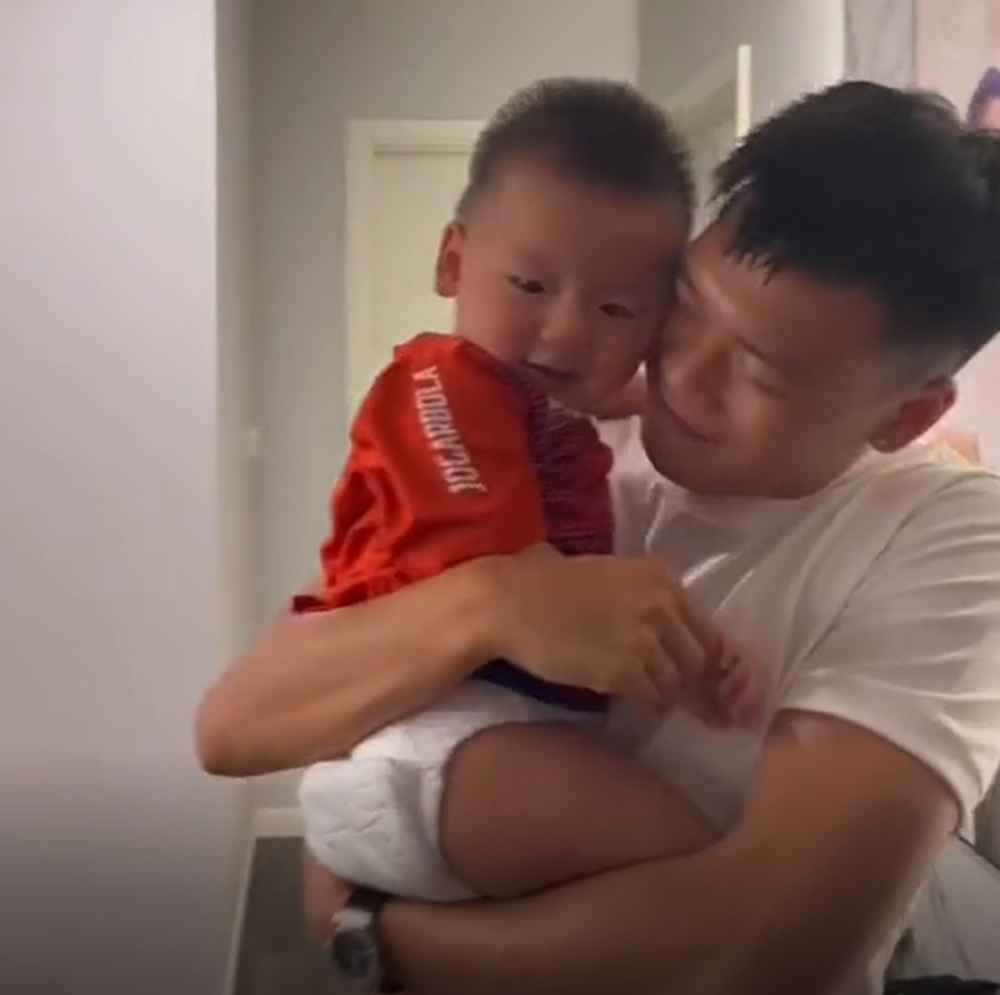 Chỉ đến khi cầu thủ sinh năm 1997 tháo kính ra, bé trai một tuổi mới chịu theo bố và để cho bố bế. Trung vệ tuyển Việt Nam ôm con vào lòng, hai bố con quấn quýt không rời.
