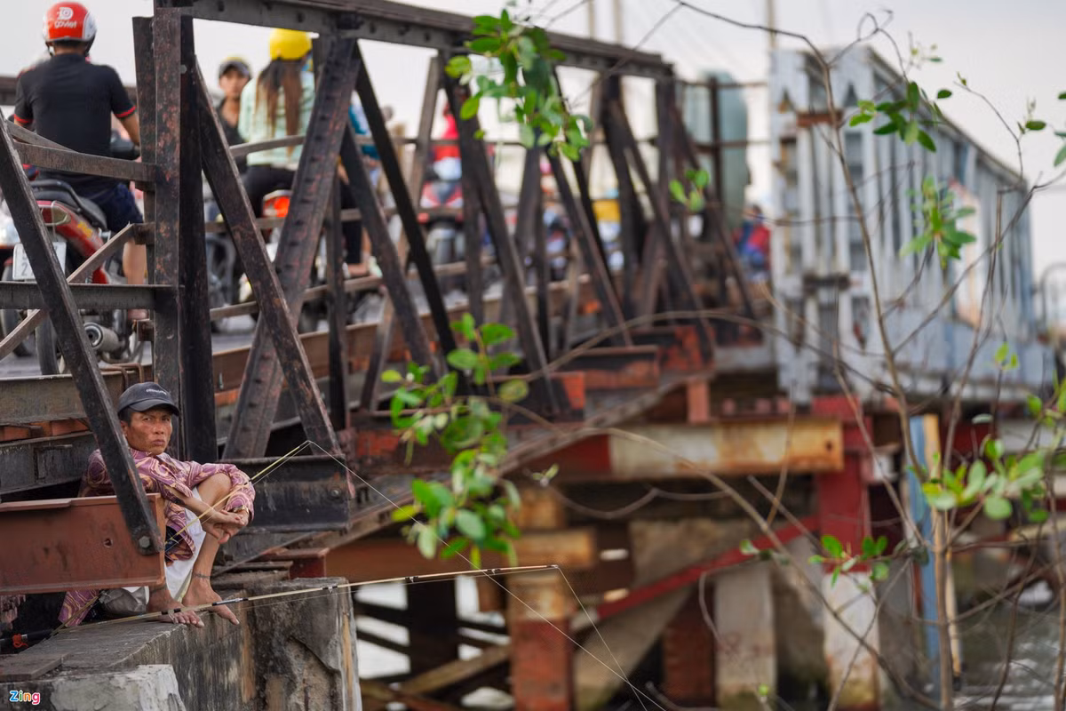 Cầu sắt đã quá cũ, người dân dễ dàng trèo qua hàng rào để ngồi câu cá trên mố cầu.