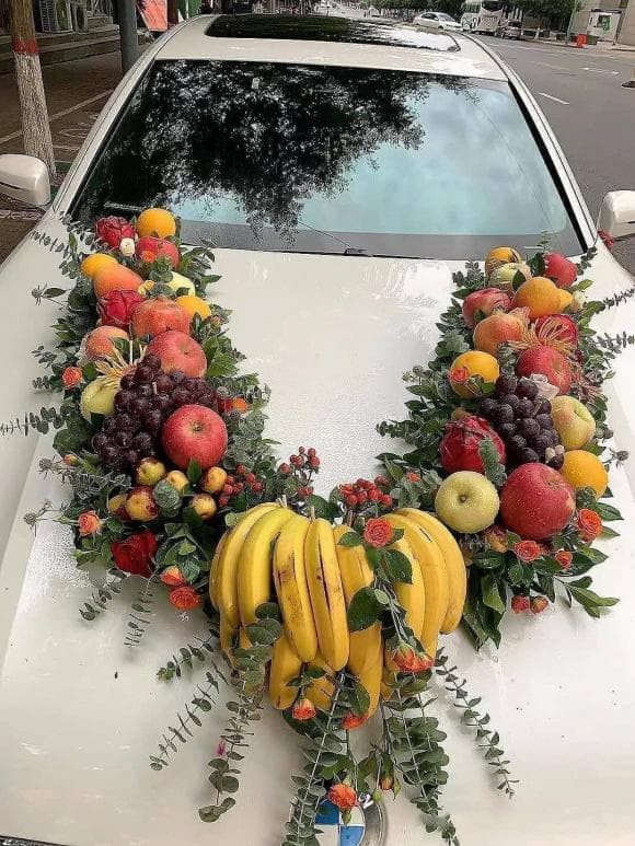 Thay vì trang trí bằng hoa tươi như cách truyền thống, xe hoa độc lạ này được thay đổi ý tưởng, trang trí bằng nhiều loại quả như nho, táo, cam... Điểm nhấn của chiếc xe đón dâu là nải chuối chín vàng ươm. Ảnh: 24h