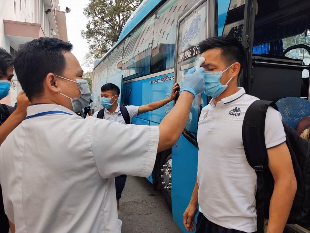 Các cầu thủ Hà Nội FC bước xuống khỏi xe buýt và ngay lập tức được đo thân nhiệt.
