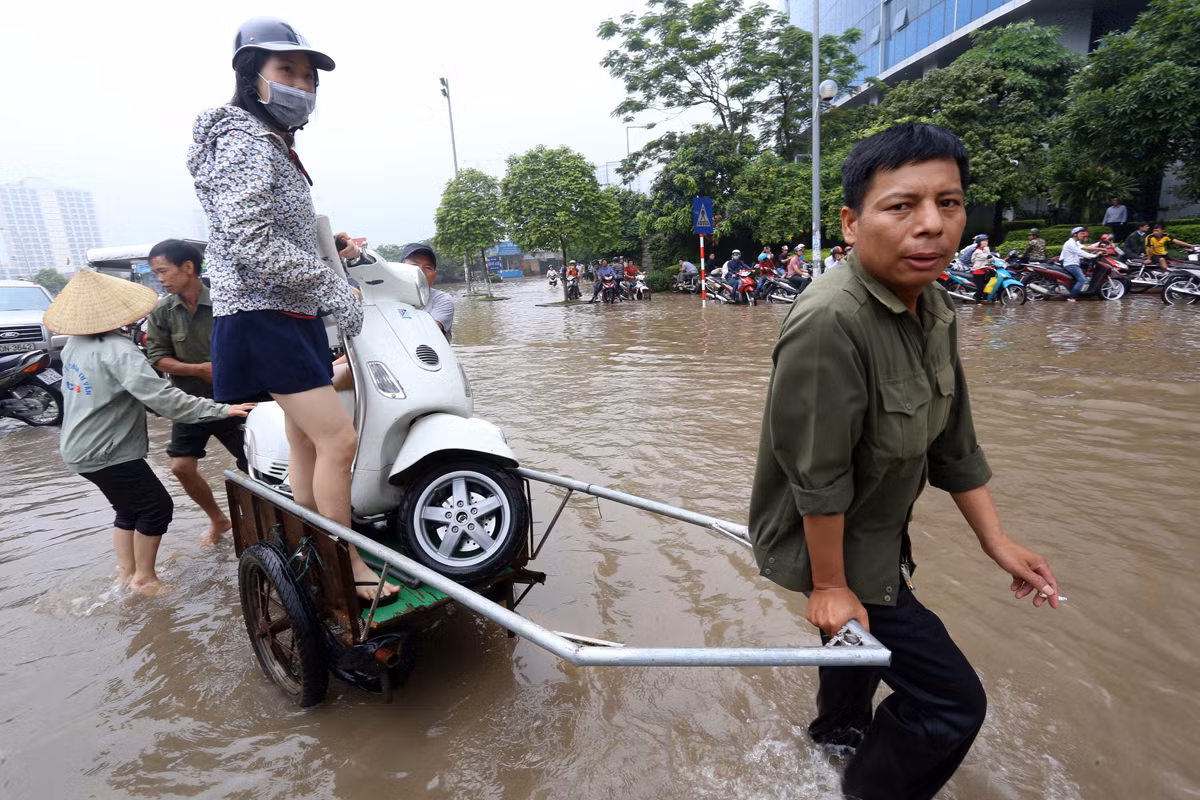 Thời điểm cuối tháng 5/2022, khi những cơn mưa lớn làm cho Hà Nội thường xuyên "chìm" trong biển nước, nhiều người đã tranh thủ mở dịch vụ "nóng" chở người, xe máy bằng xe ba gác qua những nút ngập sâu.